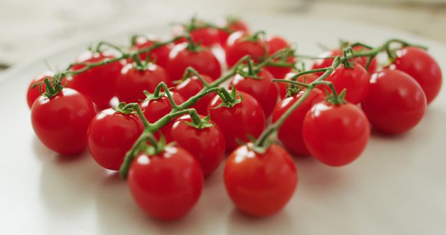 Photo showcases ripe cherry tomatoes still attached to vine, against plain background. Bright daylight highlights the freshness and vibrant red color. Ideal for use in grocery store advertisements, healthy eating blogs, and farm-to-table restaurant marketing materials.