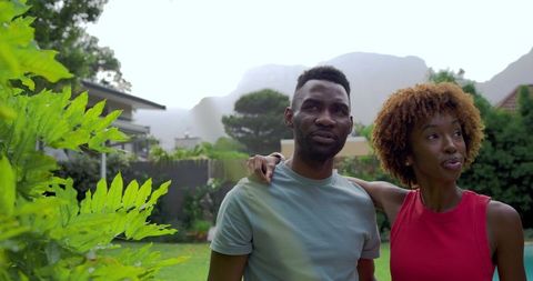 Diverse couple standing in suburban backyard sharing tranquil moment among lush greenery