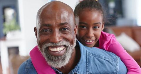African american father carrying daughter piggyback, smiling together in cozy living room