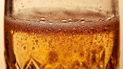 Macro Amber Drink Bubbling in Cut-Glass Tumbler with Foamy Head and Effervescence