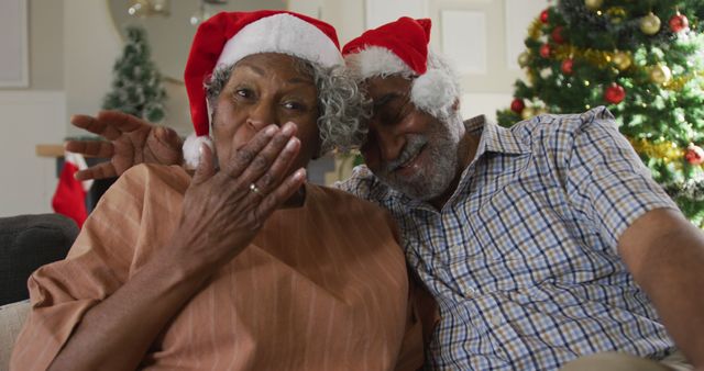 Senior couple enjoying Christmas at home, wearing Santa hats. Ideal for holiday cards, festive advertising, retirement communities promotions, family gathering articles, and lifestyle blogs focused on older adults and celebrations.