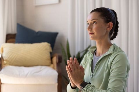 Young woman praying at home practicing mindfulness and meditation in cozy minimalist interior