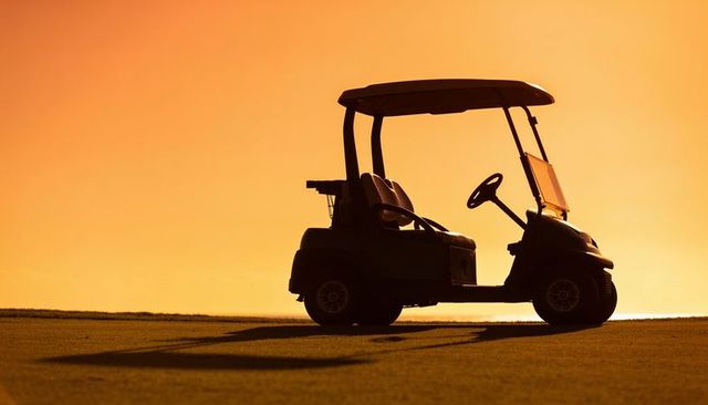 Golf cart silhouette at sunset casting long shadow on fairway with canopy and windshield