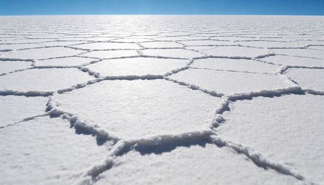 Hexagonal salt-crust tessellation stretching across vast salt flat under clear blue sky