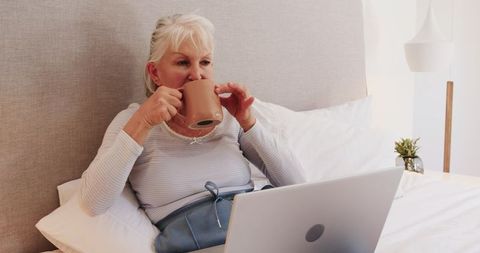 Senior Woman Relaxing in Bed with Laptop and Coffee