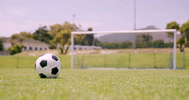 Soccer ball on grassy field with goalposts in background under clear sky. Ideal for sports promotions, recreational activity visuals, training programs, and motivational posters.