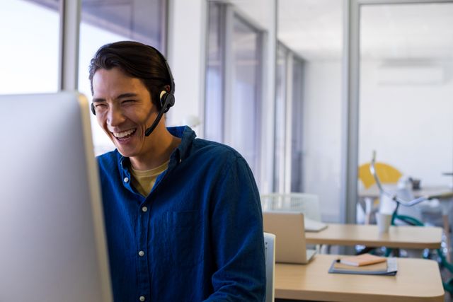 Male executive wearing headset working at desk in modern office. Ideal for illustrating customer service, corporate communication, professional work environment, and business technology.