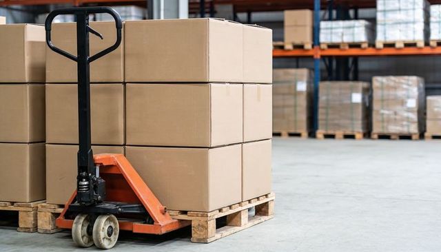 Manual Pallet Jack Lifting Stacked Cardboard Boxes on Wooden Pallet in Warehouse Logistics