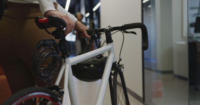 Person standing in well-lit modern office hallway holding a bicycle. Perfect for use in articles or advertisements about sustainable transportation, eco-friendly commuting, carefree modern workplaces, or urban lifestyle.