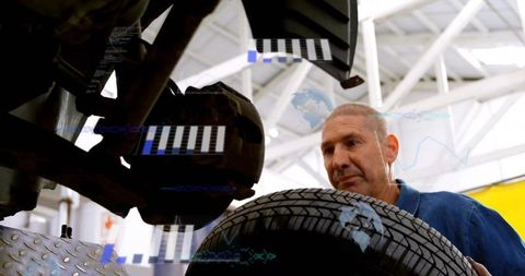 Experienced mechanic inspecting tire and brake assembly with digital overlay in garage