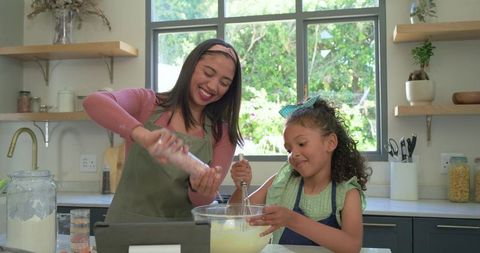 Smiling mother and daughter whisking batter together in bright modern kitchen for family baking
