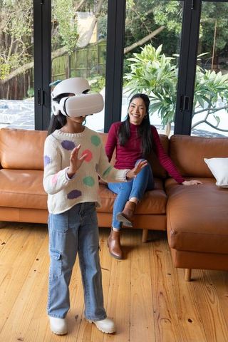 Asian mother watching child playing with virtual reality headset in sunlit living room