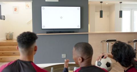 Diverse friends watching mounted tv test pattern holding soccer ball in living room