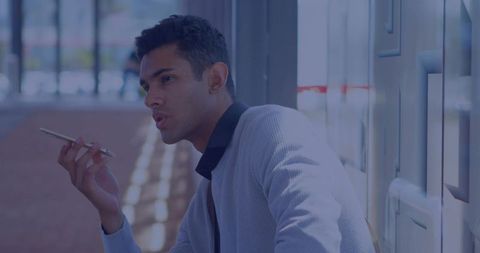 Indian professional speaking into smartphone by window in corridor wearing gray jacket