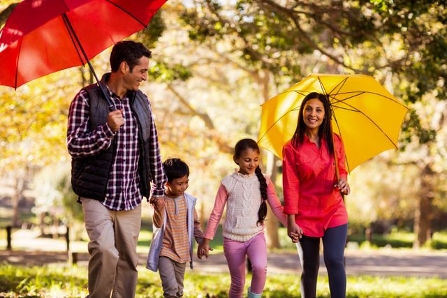 Family enjoying a walk in the park during autumn, holding colorful umbrellas. Ideal for concepts of family bonding, outdoor activities, seasonal changes, and leisure time. Perfect for advertisements, family-oriented content, and lifestyle blogs.
