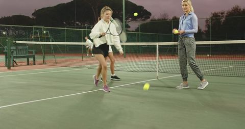 Evening tennis practice with instructor coaching diverse foursome on outdoor court