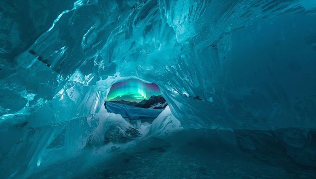 Aurora framing through turquoise glacial ice arch over frozen cavern