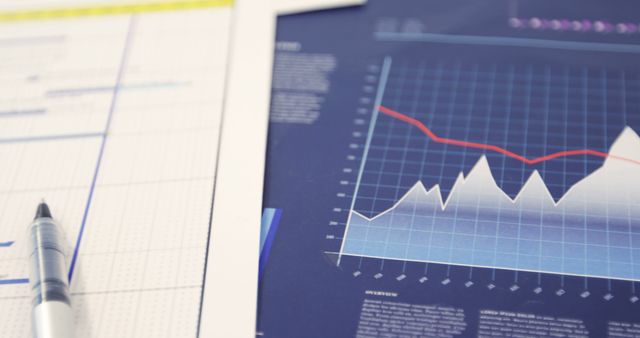 Close-up of financial graphs and charts with a pen on a desk. Graph showcases market trends with lines and bars. Useful for illustrating business reports, financial analysis, investment strategies, and economic data presentations.