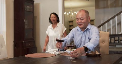 Senior Man Enjoying Dinner with Wine, Woman Entering Room