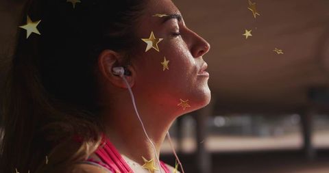 Focused woman catching breath after workout wearing wired earphones with gold star overlay
