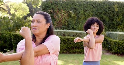 Women stretching arms outdoor in lush garden setting