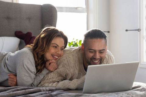 Couple relaxing on bed watching laptop together for cozy streaming and weekend bonding