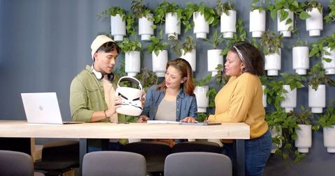 Diverse team examining virtual reality headset at modern coworking bar with living wall