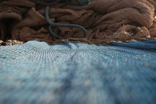Close-up of blue fishing nets and ropes on a boat. The photo captures the detailed texture and intricate patterns of the nets, symbolizing the fishing industry. Ideal for use in articles or advertisements related to fishing, marine life, fisheries, outdoor activities, or boating. The image can also be used to highlight traditional fishing methods and coastal community livelihoods.