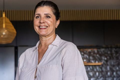 Mature woman smiling in modern kitchen wearing beige linen shirt warm natural light