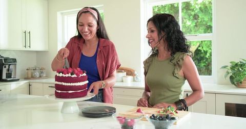 Friends cutting red velvet cake on bright modern kitchen island celebrating together