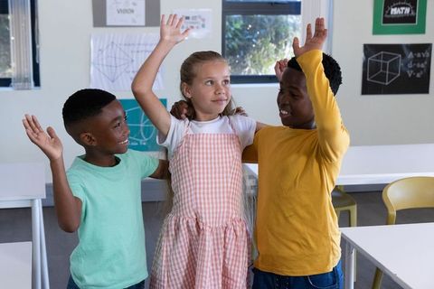 Multicultural elementary students raising hands in classroom collaborating on geometry