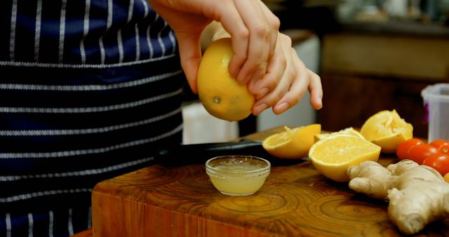 Person seen squeezing lemon juice over a small bowl on a wooden cutting board, surrounded by various fresh ingredients including ginger and tomatoes. Ideal for use in cooking blogs, recipe book illustrations, healthy eating promotions, and culinary classes.