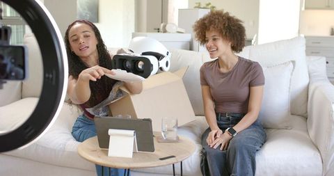 Two Friends Unboxing and Demonstrating White VR Headset on Sofa with Tablet and Ring Light
