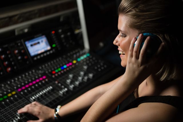 This image depicts a female audio engineer using a sound mixer in a recording studio. Perfect for articles about music production, audio engineering, professional women in technology, or the creative industry. It can also be used for promotional materials for recording studios, audio equipment, or educational courses in sound engineering.