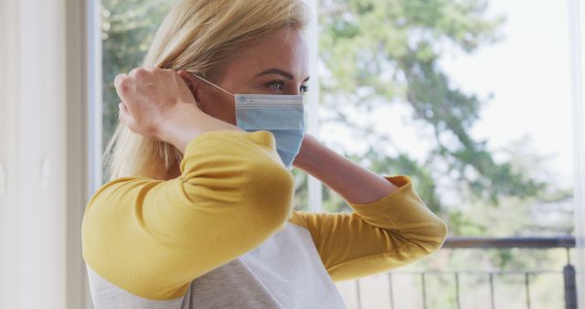 Woman Putting On Medical Mask by Window at Home - Download Free Stock Images Pikwizard.com