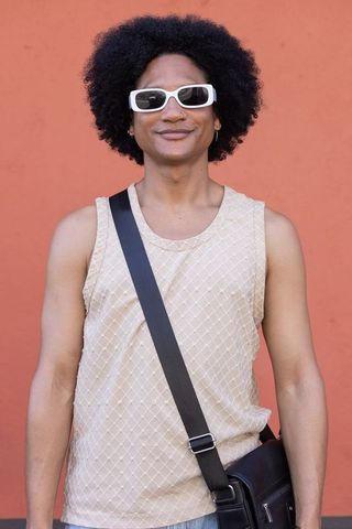 Confident african american man wearing white sunglasses, beige tank, crossbody bag, terracotta wall