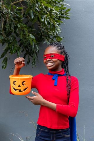 African american teen girl smiling in superhero costume holding halloween bucket