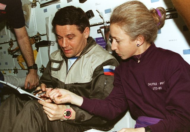 NASA astronaut and Mir cosmonaut collaborating during an STS-81 mission in Space Shuttle Atlantis, January 1997. Highlighting international cooperation in space. Perfect for articles on space exploration, international cooperation, and NASA history.