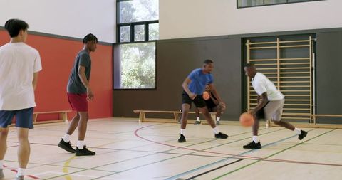 High-intensity indoor basketball pickup game with young men dribbling and defending