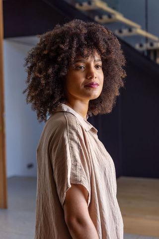 African woman standing in modern interior near staircase, soft natural light portrait, calm
