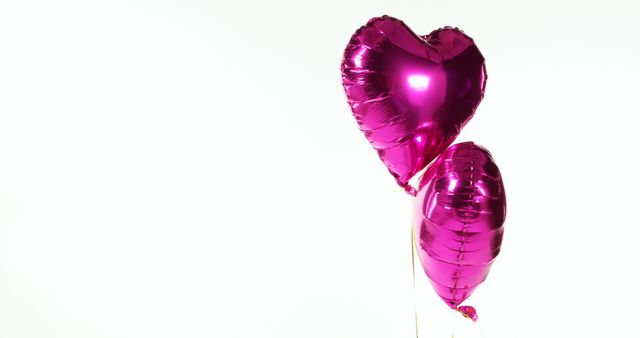 Two purple heart-shaped balloons floating together on a white background, creating a simple yet festive feel. Perfect for use in marketing materials focused on celebrations, romantic occasions such as Valentine's Day, party invitations, greeting cards, or as a decorative element for various festive events.