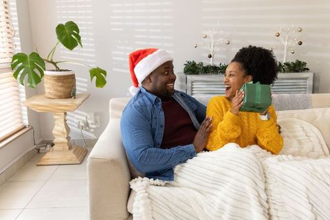 African american couple laughing and exchanging green gift on cozy christmas couch