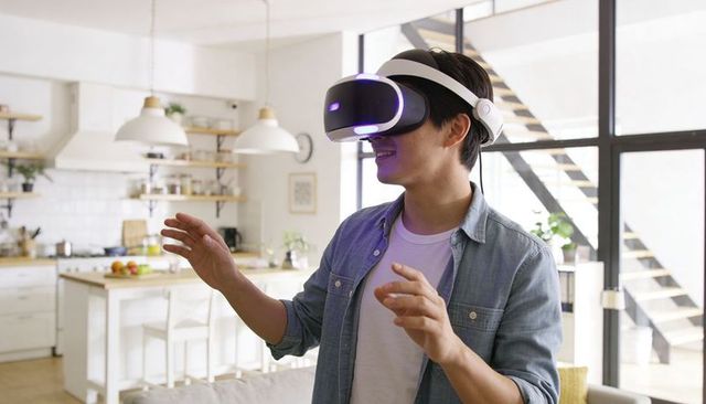 Asian man wearing vr headset interacting with virtual interface in modern open-plan home