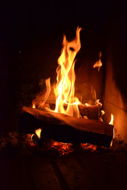 Burning logs in a fireplace create warm, cozy ambiance perfect for homes, cabins and rustic settings. This visual can be used in articles and advertisements related to home comfort, seasonal content, camping trips, fireplace safety, and cozy interior design.