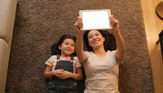Mother and daughter lying on plush brown rug holding tablet and enjoying family time