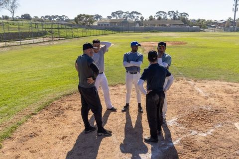 Coach discussing lineup with baseball team on pitchers mound during sunny practice