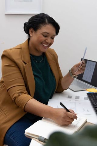 African american professional smiling while writing in notebook at bright organized desk
