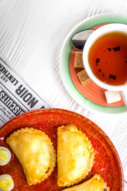 Pastries and a cup of tea presented on a white wooden table, perfect for food blogs, breakfast menus, and cozy dining advertisements. The image emphasizes a morning meal setting with a newspaper and carefully arranged food items inviting a relaxed, leisurely feel.