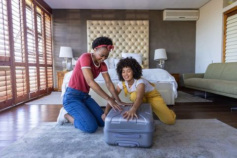 Diverse friends packing suitcase together in modern bedroom preparing for trip