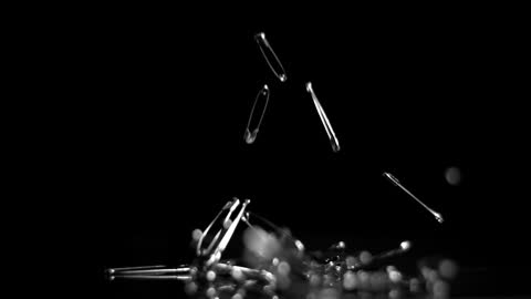 Safety Pins Falling in Slow Motion on Black Background
